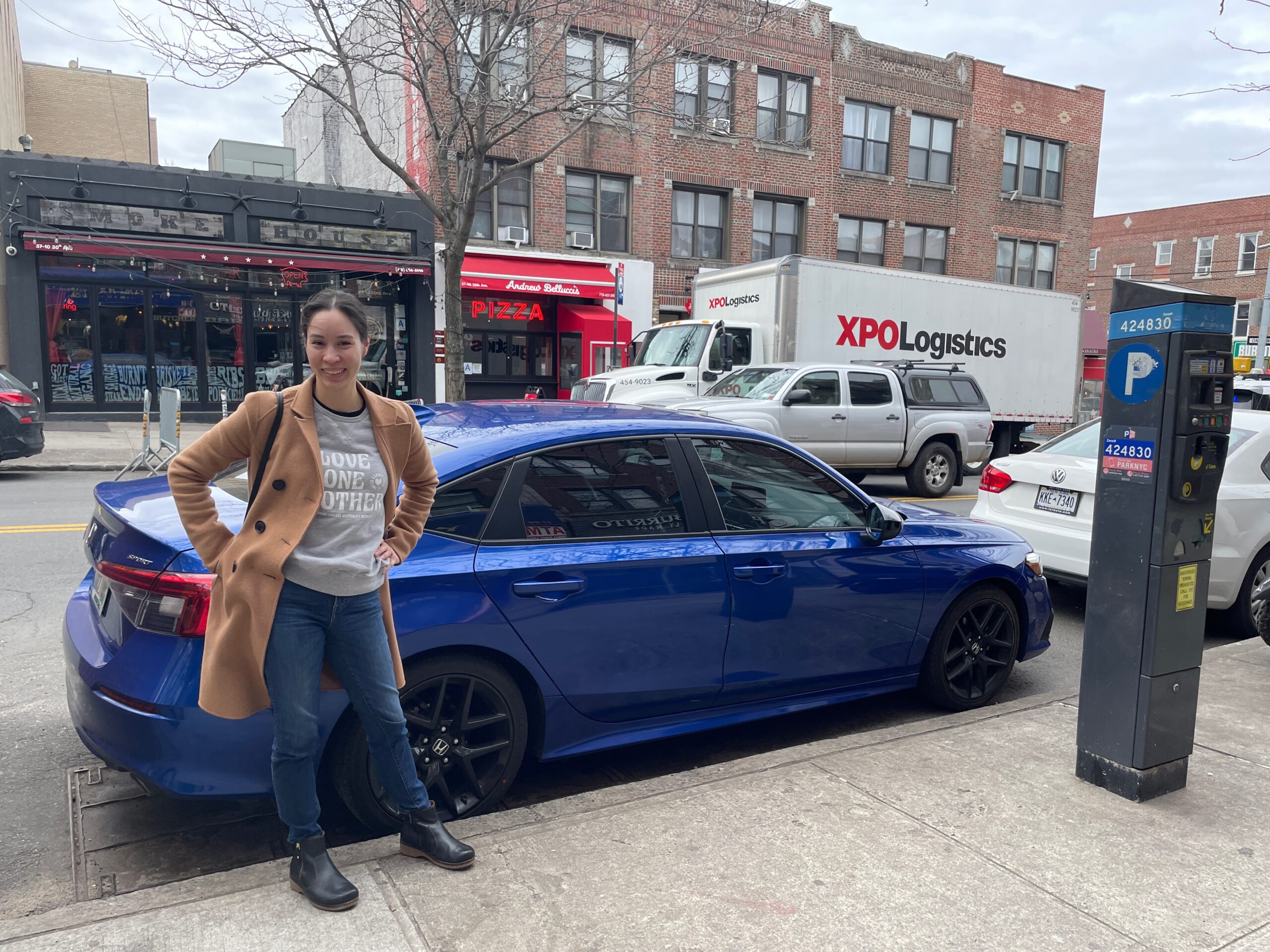 Allison standing in front of a parallel parked blue car